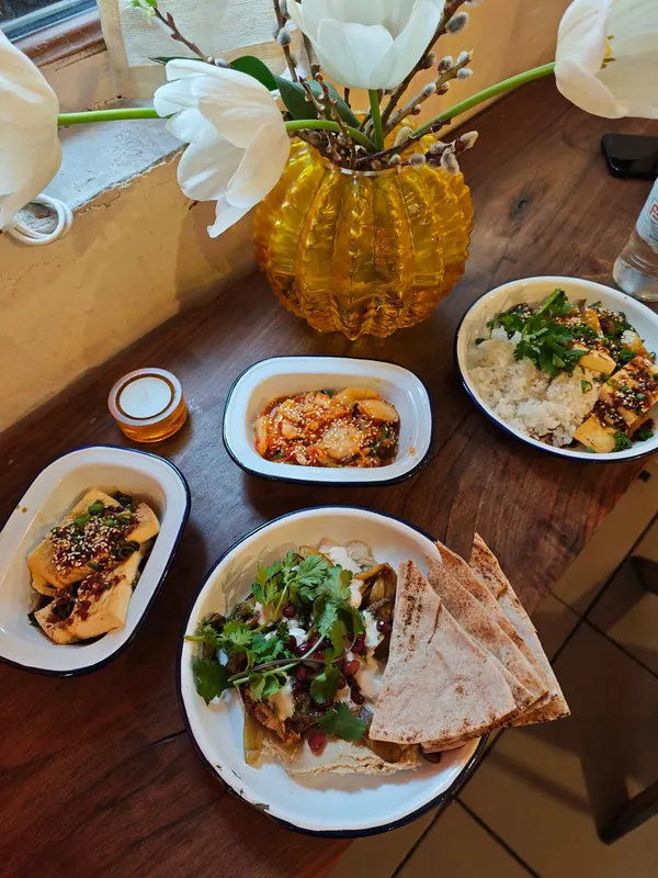 A table full of enamel bowls: hummus, kimchi, rice and salads