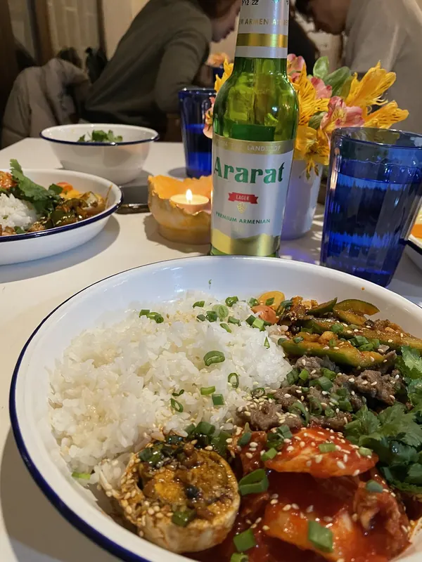 A bowl of rice, bulgogi and kimchi next to a bottle of Ararat lager